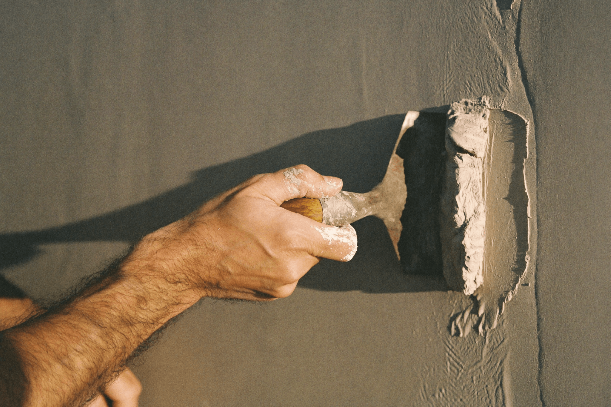 Hands finishing wet lime plaster with a steel trowel.